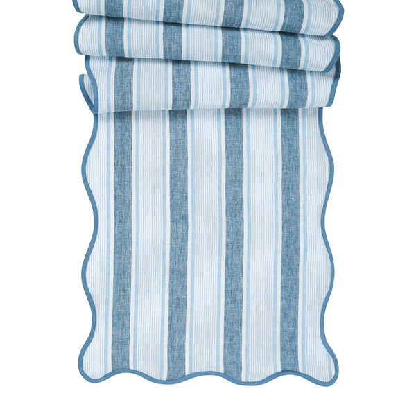 The Juliska Cabana Stripe Tabletop Collection features a folded fabric with blue and white cabana stripes, scalloped trim, and wavy edges.