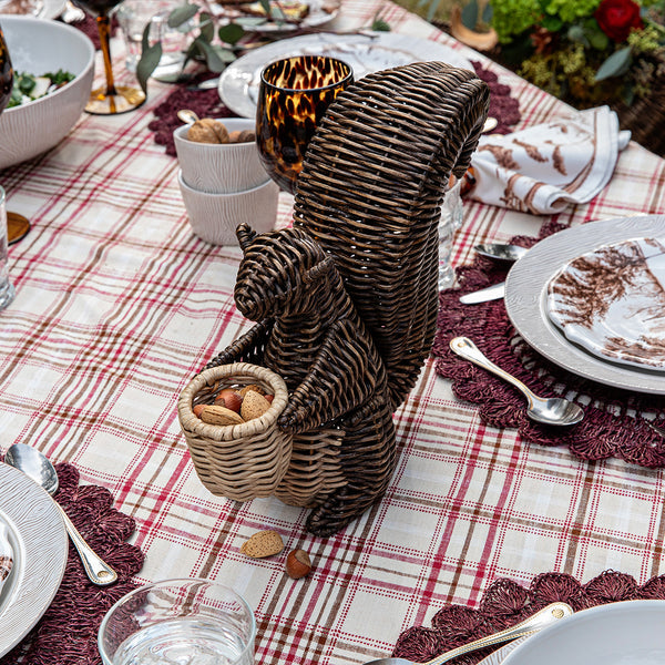 The Juliska Devon Willow Squirrel Flameless Candle Holder serves as a charming centerpiece on a plaid tablecloth, surrounded by plates, glasses, and utensils on the dining table.