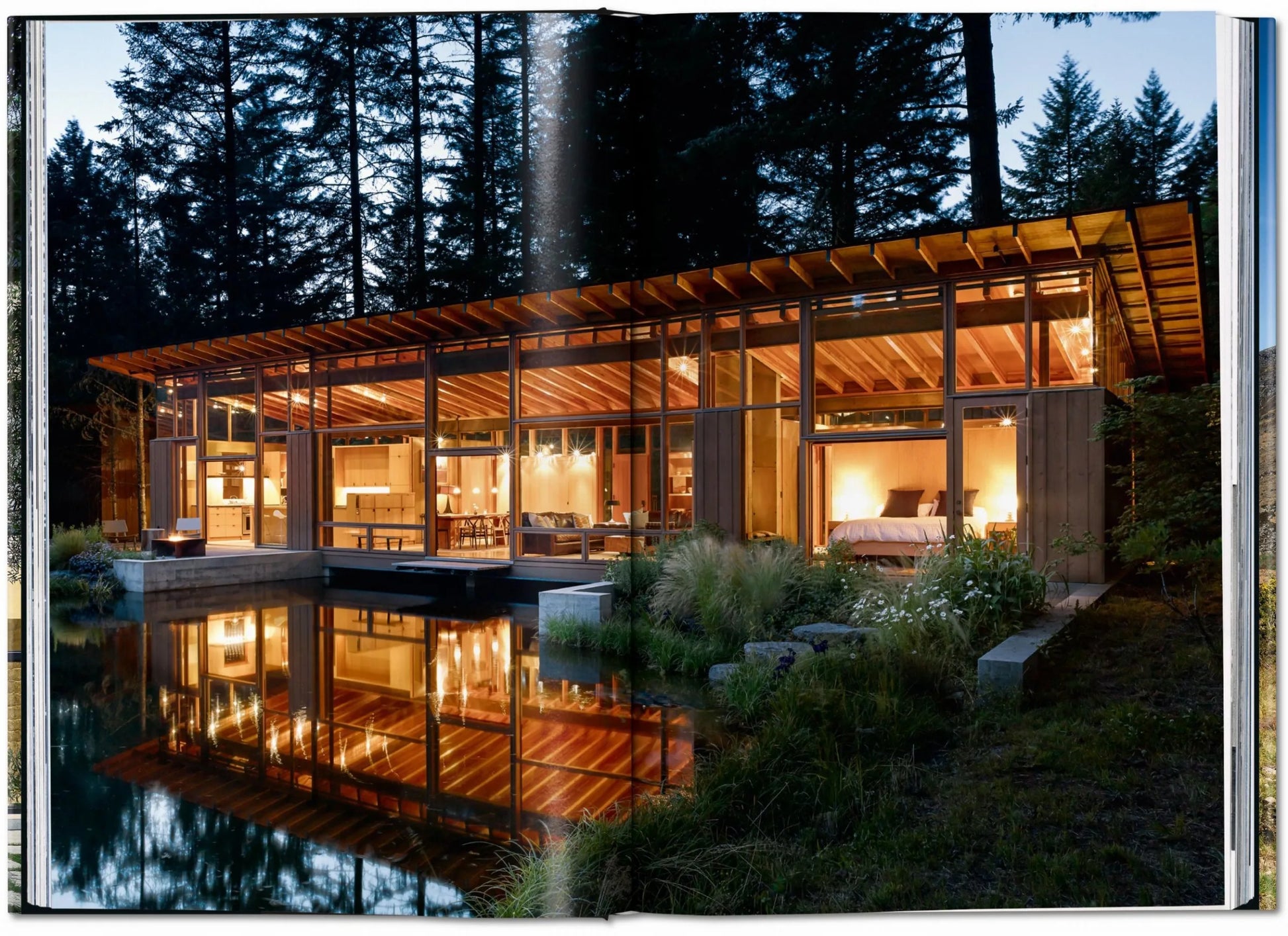 The book "Homes For Our Time" by Taschen showcases stunning modern architecture, like glass houses with warm lighting, tree surrounds, and serene pond reflections—a beautiful example of contemporary home design.