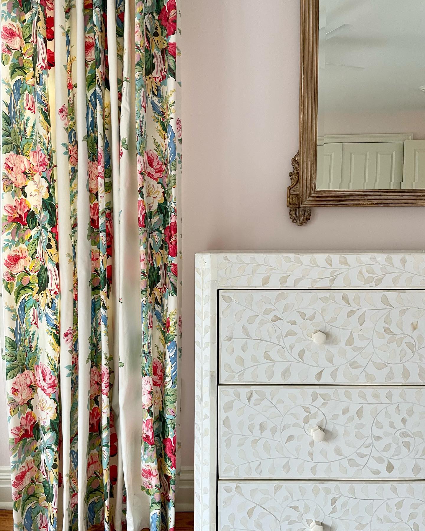 Floral curtains beside a Made Goods Lexi Dresser featuring an Indian leaf pattern; a framed mirror is partially visible on the pale pink wall.