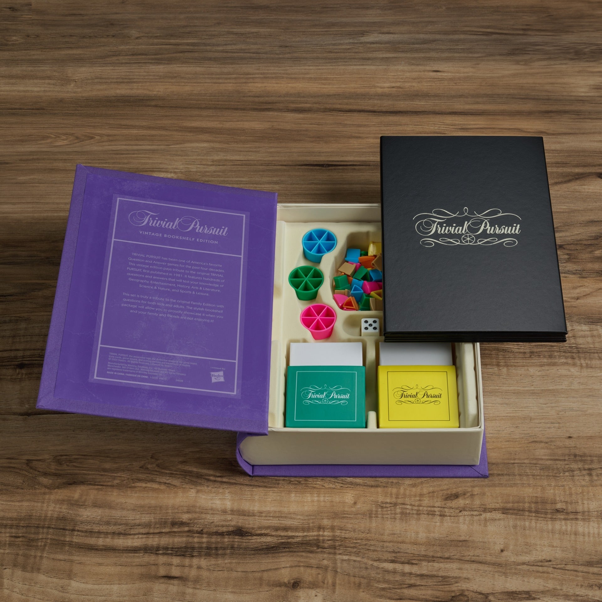 Unveil the Trivial Pursuit Vintage Bookshelf Edition by WS Game Company, showcasing a vibrant assortment of question and answer cards, game pieces, a die, and the board on a wooden surface.