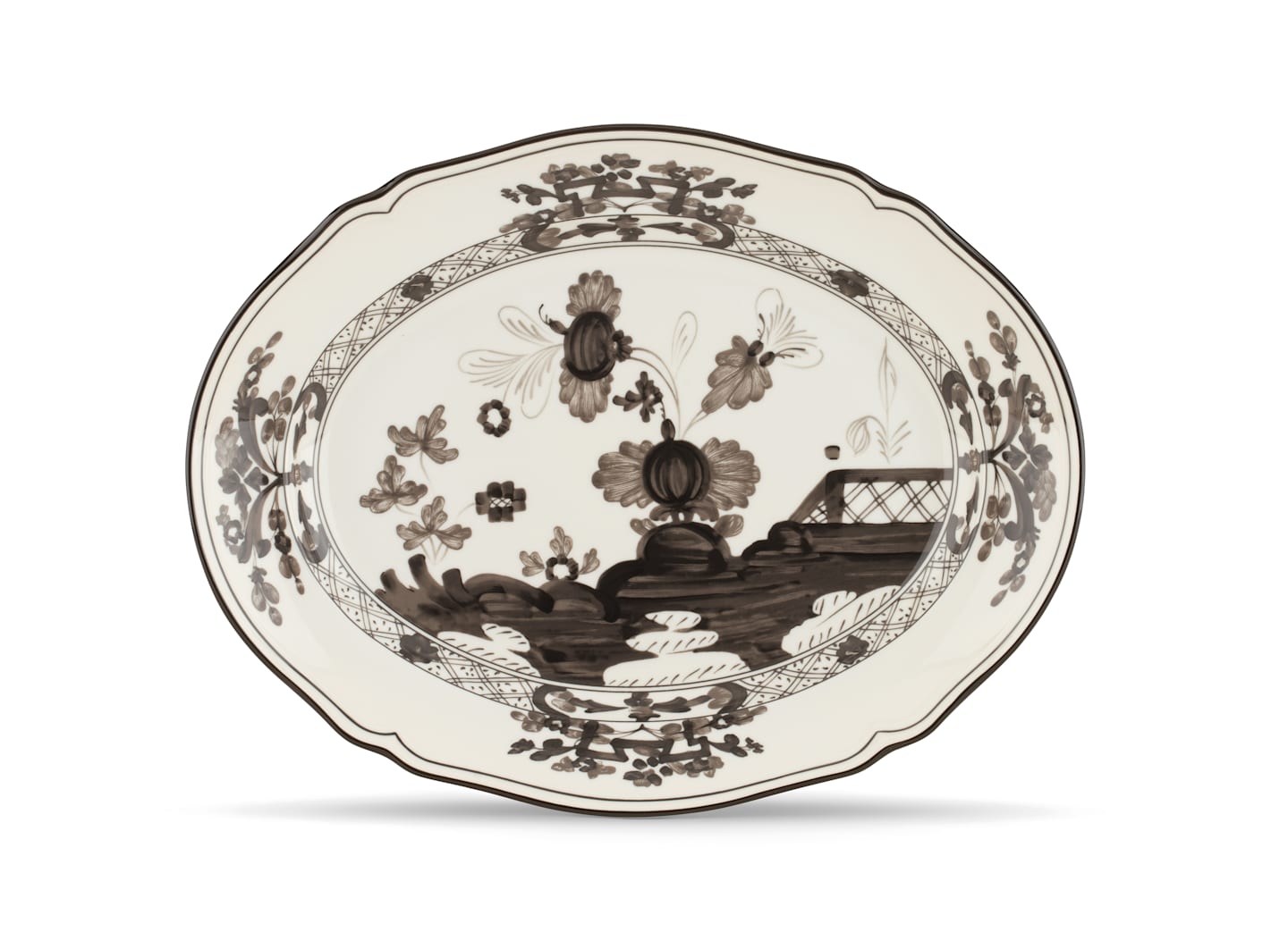The Oriente Italiano Albus Dinnerware Collection by Ginori 1735 features ornate porcelain plates with scalloped edges, adorned with black floral and landscape patterns on a white background.
