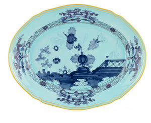 The Ginori 1735 Oriente Italiano Iris Oval Platter is a blue and white porcelain plate with floral and architectural motifs, accented by a decorative yellow rim.