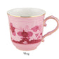 A pink ceramic mug with floral patterns, gold rim, and curved handle showcases Italian elegance by Ginori 1735 as part of the Oriente Italiano Porpora Dinnerware Collection. "Mug" is labeled below the image.