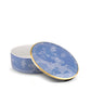 A round blue porcelain box from Ginori 1735’s Oriente Italiano Pervinca collection features white floral patterns and a gold-edged lid, displayed partially open on a white background.