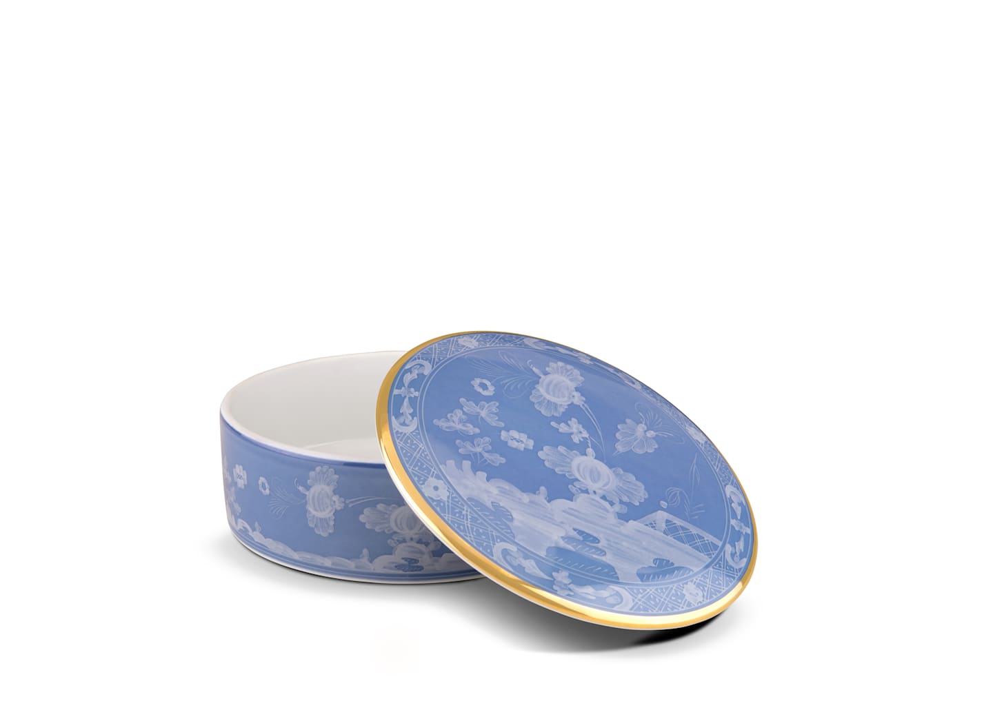 A round blue porcelain box from Ginori 1735’s Oriente Italiano Pervinca collection features white floral patterns and a gold-edged lid, displayed partially open on a white background.