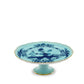 The Ginori 1735 Oriente Italiano Iris with Gold Cake Stand features light blue porcelain, a gold-trimmed edge, and a blue floral motif inspired by Faenza ceramics, set against a white background.