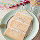 The Hester & Cook Cake Slice Table Accent, shaped like a birthday cake slice with "MAKE A WISH!", serves as charming table decor beside a glass holding an ice cream cone with sprinkles and colorful straws.