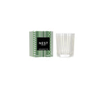 The Nest Birchwood Pine Collection holiday candle, shown in a clear, patterned glass jar beside its green and white box, evokes the crisp fragrance of a winter forest.