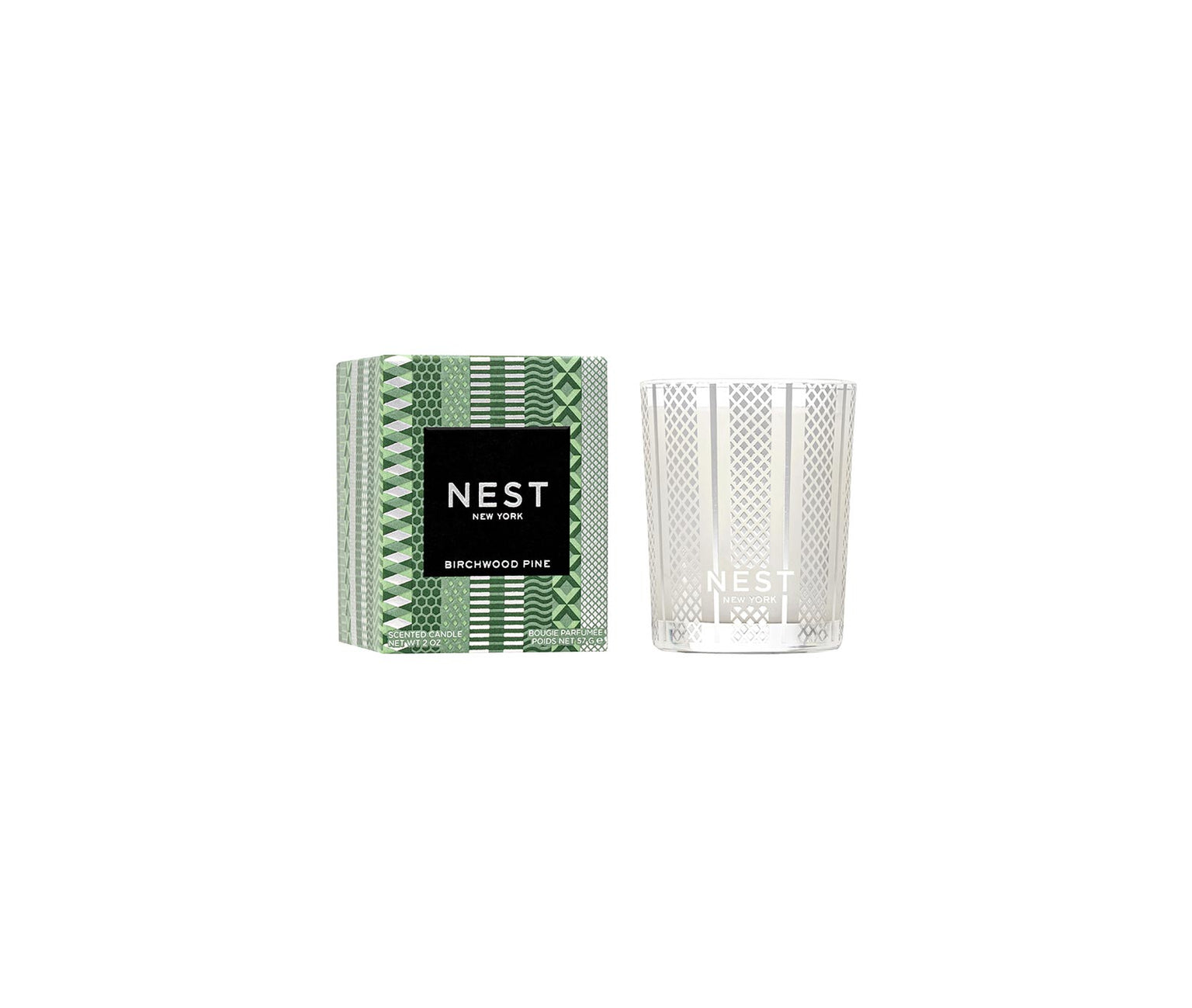 The Nest Birchwood Pine Collection holiday candle, shown in a clear, patterned glass jar beside its green and white box, evokes the crisp fragrance of a winter forest.