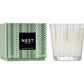A Nest Birchwood Pine Collection holiday candle in a patterned glass sits beside its green and white box, evoking the fresh, wintry scent of a forest.