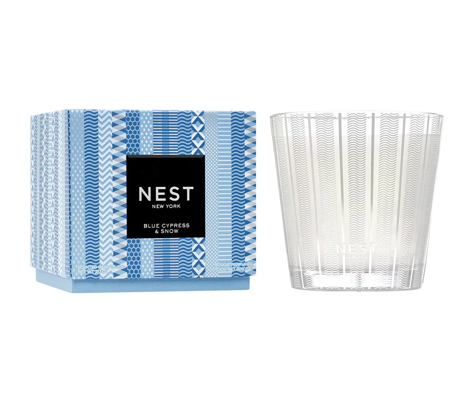 A Nest Blue Cypress & Snow Collection candle in a patterned blue box (left) and clear textured glass holder (right), offering a winter scent with smoked vanilla bean notes.