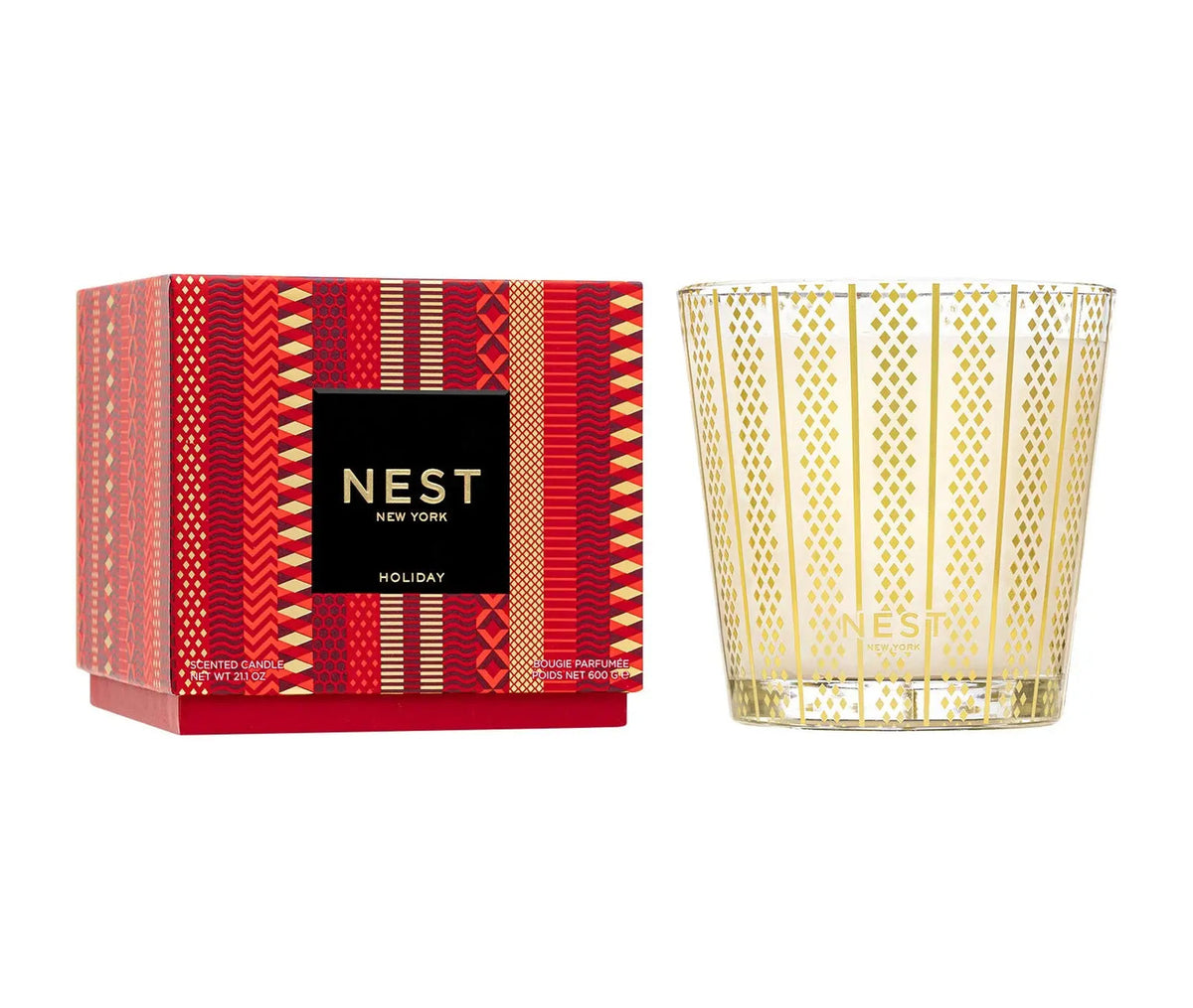 A red patterned NEST Holiday Collection fragrance box sits next to a glass candle vessel with a gold geometric design.