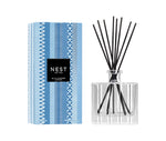 The Nest Blue Cypress & Snow Collection reed diffuser features a patterned glass bottle with black reeds and comes in a blue and white geometric box—ideal for adding a cozy winter scent to your space.