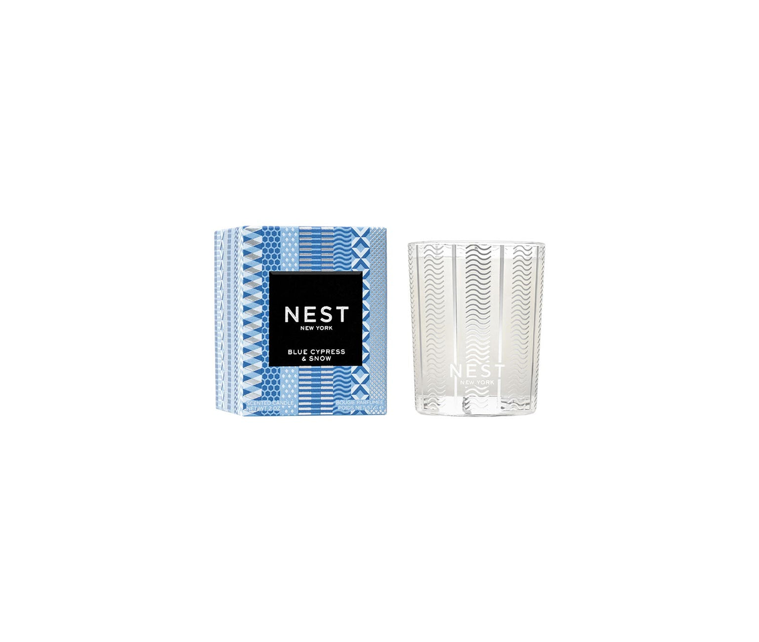 A Nest Blue Cypress & Snow Collection candle with smoked vanilla bean winter scent, in a clear glass holder next to its blue and white patterned box featuring a black label.