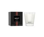 A Nest Something Tropical Candle from the Candle and Diffuser Collection is shown in a white glass container beside its black box, with passion fruit notes delivering a vibrant fragrance.