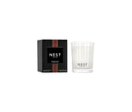 The Nest Something Tropical Candle from the Candle and Diffuser Collection sits in a clear glass jar beside its black box, offering vibrant passion fruit and soft cashmere woods notes for an inviting fragrance experience.