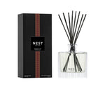 The Nest Something Tropical Candle and Diffuser Collection features a sleek black box and clear reed diffuser, both with matching labels, capturing the essence of passion fruit and cashmere woods.