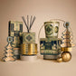 Pierre Marie Birchwood Collection home fragrance products, including a reed diffuser, 3-wick candle, and boxed items, arranged with gold-toned geometric and tree-shaped ornaments.