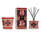 A Nest Pierre Marie Holiday Collection pomegranate pine 3-wick candle in a patterned glass jar, a decorative box, and a square reed diffuser with ornate red, gold, and blue holiday-themed designs.