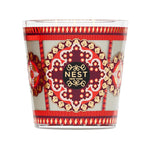 A 3-wick Nest Pierre Marie Holiday Collection pomegranate pine candle in a glass holder featuring a patterned red, gold, and grey design with a central decorative emblem.