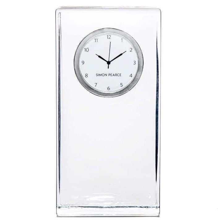 The Woodbury Tall Clock by Simon Pearce features a rectangular clear glass body, a round white face with black hour and minute hands, and "Simon Pearce" elegantly printed on the dial.
