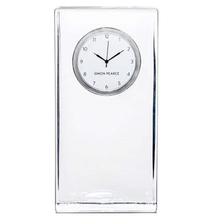 The Woodbury Tall Clock by Simon Pearce features a rectangular clear glass body, a round white face with black hour and minute hands, and "Simon Pearce" elegantly printed on the dial.