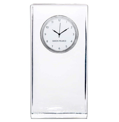 The Woodbury Tall Clock by Simon Pearce features a rectangular clear glass body, a round white face with black hour and minute hands, and "Simon Pearce" elegantly printed on the dial.