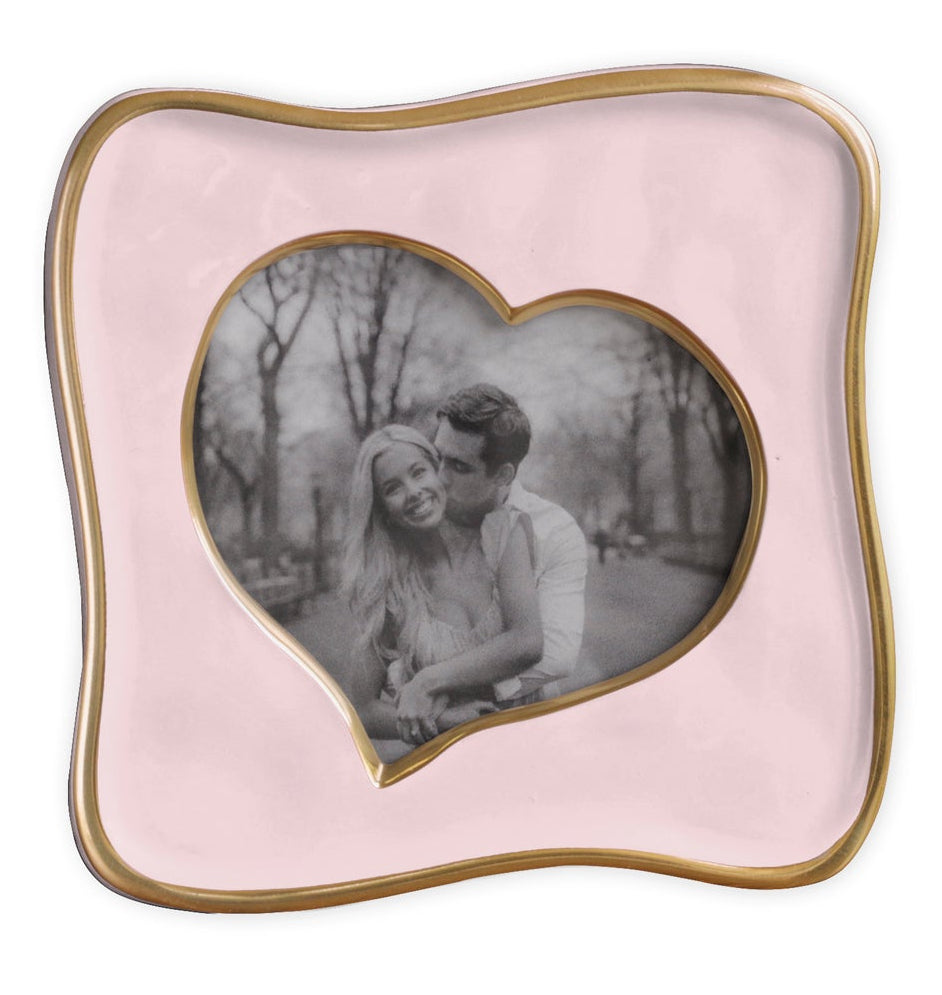 Black-and-white photo of a smiling couple in a park, displayed in the Beatriz Ball Encanto Curved Heart Frame Collection, 5x5—a pink handcrafted heart-shaped frame with a wavy gold border.
