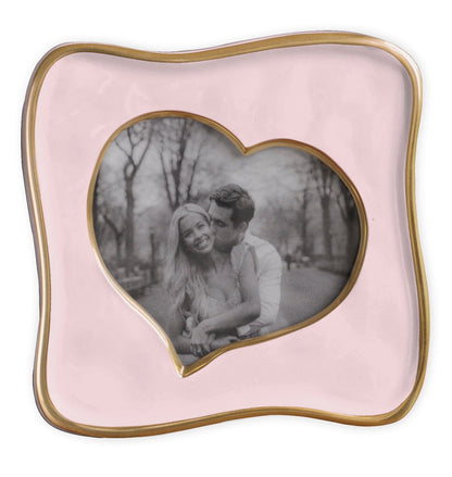 Black-and-white photo of a smiling couple in a park, displayed in the Beatriz Ball Encanto Curved Heart Frame Collection, 5x5—a pink handcrafted heart-shaped frame with a wavy gold border.