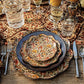 A table setting featuring Juliska’s Willa Dinnerware Collection with layered floral-patterned plates, a scalloped charger, silver cutlery, glassware, and a decorative patterned tablecloth.