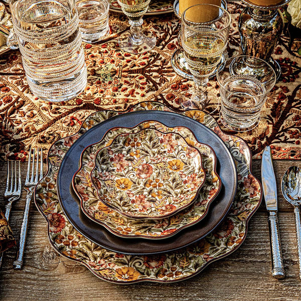 A table setting featuring Juliska’s Willa Dinnerware Collection with layered floral-patterned plates, a scalloped charger, silver cutlery, glassware, and a decorative patterned tablecloth.