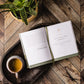 Resilient Hope by Thomas Nelson/Harper Collins rests open on a wooden tray with tea, glasses, and a potted plant on a herringbone table—creating an atmosphere of encouragement and strength.