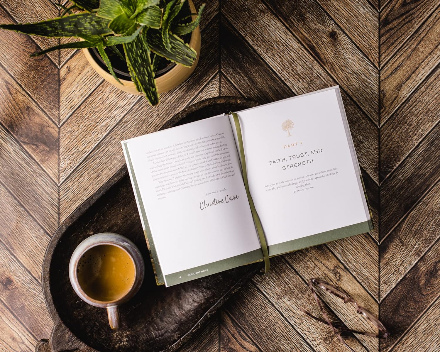 Resilient Hope by Thomas Nelson/Harper Collins rests open on a wooden tray with tea, glasses, and a potted plant on a herringbone table—creating an atmosphere of encouragement and strength.