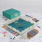 Experience the Monopoly Del Mar Shagreen Edition by WS Game Company, a luxurious board game featuring a teal and gold design with faux-sharkskin textures for an extraordinary touch. This exquisite set includes high-quality components such as property cards, dice, houses, hotels, and a storage box crafted on a marble surface that exudes oceanic vibes.