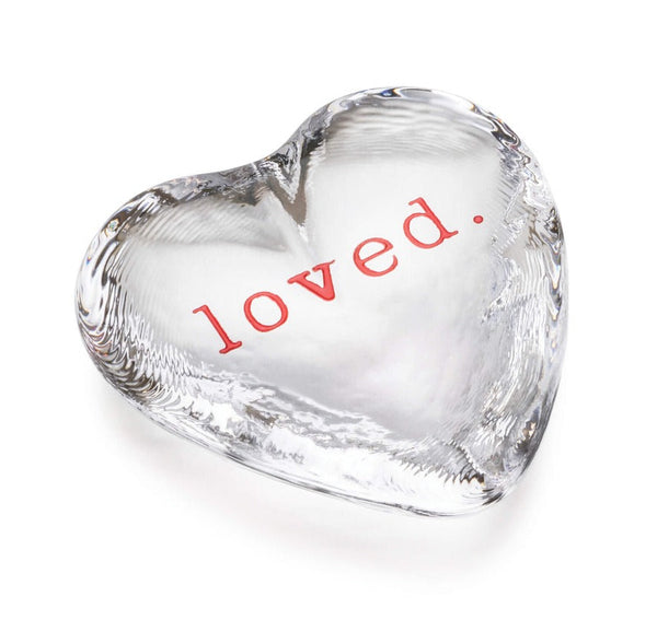 The Simon Pearce "loved" Highgate Heart is handcrafted from lead-free glass and features the word "loved" in bold red text on a crystal-clear heart-shaped surface.