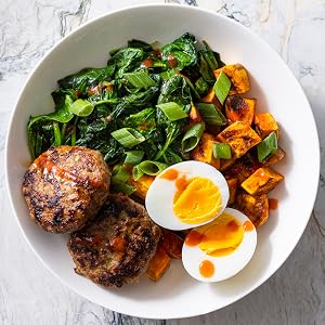 Discover inspiring meal ideas in *The Complete High-Protein Cookbook* from Penguin Random House, featuring dishes like white bowls filled with meat patties, sautéed greens, roasted sweet potatoes, and a soft-boiled egg topped with sauce and green onions—ideal for anyone seeking high-protein meals or looking to add variety to their healthy eating plans.