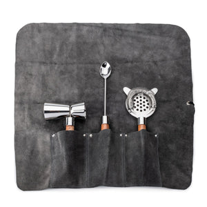 The Simon Pearce Acacia Bar Tool Set includes a gray suede roll-up pouch with separate pockets for a double-sided jigger, bar spoon, and julep strainer, each featuring wooden handles.