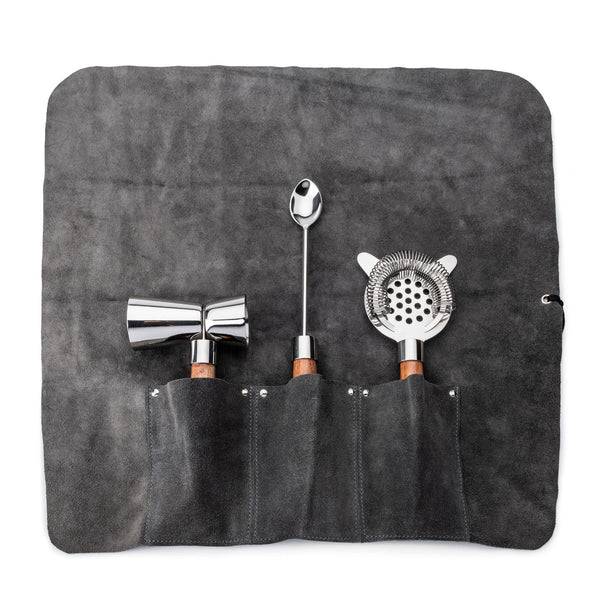 A Simon Pearce Acacia Bar Tool Set featuring three stainless steel bar tools—a jigger, spoon, and strainer—neatly displayed in a grey leather roll-up case with slots.