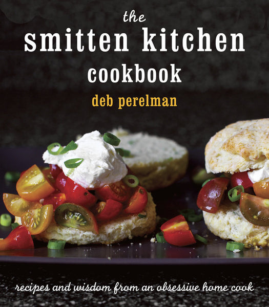 Cover of "The Smitten Kitchen Cookbook" by Penguin Random House showcases a biscuit with cherry tomatoes and cream on a dark background, reflecting the charm of accessible home cooking through Deb Perelman's delightful recipes.