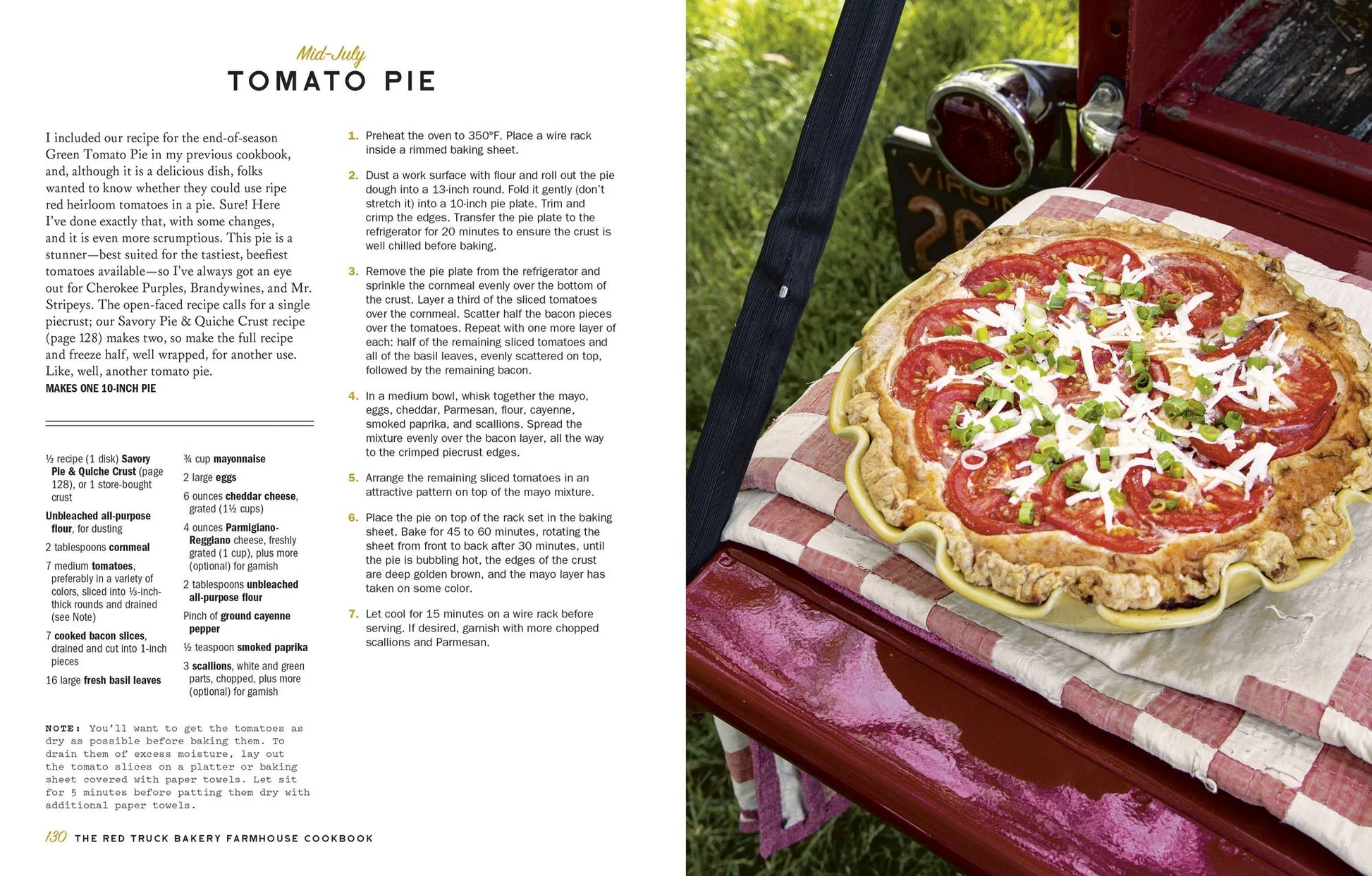 A golden-crusted tomato pie rests on a red and white checkered cloth atop a vibrant red surface outdoors, accompanied by a knife and surrounded by lush green grass, capturing the cozy spirit of recipes featured in The Red Truck Bakery Farmhouse Cookbook from Penguin Random House.