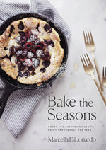 A cherry clafoutis in a skillet on a striped cloth beside three forks, showcased on the cover of Bake the Seasons from Penguin Random House, beautifully captures the comforting and welcoming essence of the seasonal baking recipes featured throughout the book.