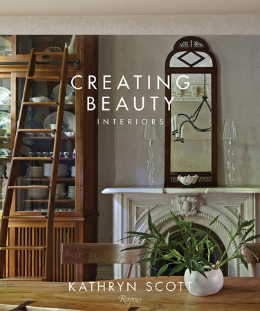 Cover of the book "Creating Beauty: Interiors" by Rizzoli. Shows a minimalist living space with a fireplace, mirror, wooden bookshelf with ladder, and a table with a plant, featuring artisanal details.