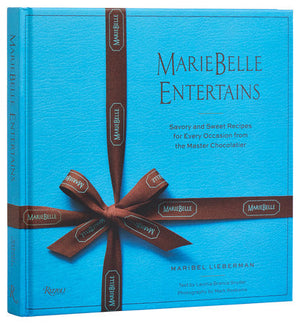 Blue book titled "Mariebelle Entertains: Savory and Sweet Recipes" by Rizzoli, features chocolate desserts and entertaining recipes with text by Lunella Brennan, photography by Mark Roskams, and authored by Maribel Lieberman; includes a brown ribbon design.