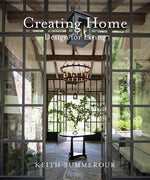 Book cover of “Creating Home, Design for Living” by Rizzoli, a renowned architecture book, showcasing a glass-walled room with a round table and chandelier, overlooking an outdoor view that reflects the timeless charm of Southern homes.