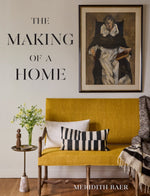 Yellow bench with cushions and blanket, side table with flowers, framed portrait above, and Meridith Baer: The Making of a Home by Abrams—a showcase of elegant home staging.
