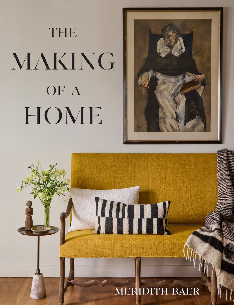Yellow bench with cushions and blanket, side table with flowers, framed portrait above, and Meridith Baer: The Making of a Home by Abrams—a showcase of elegant home staging.