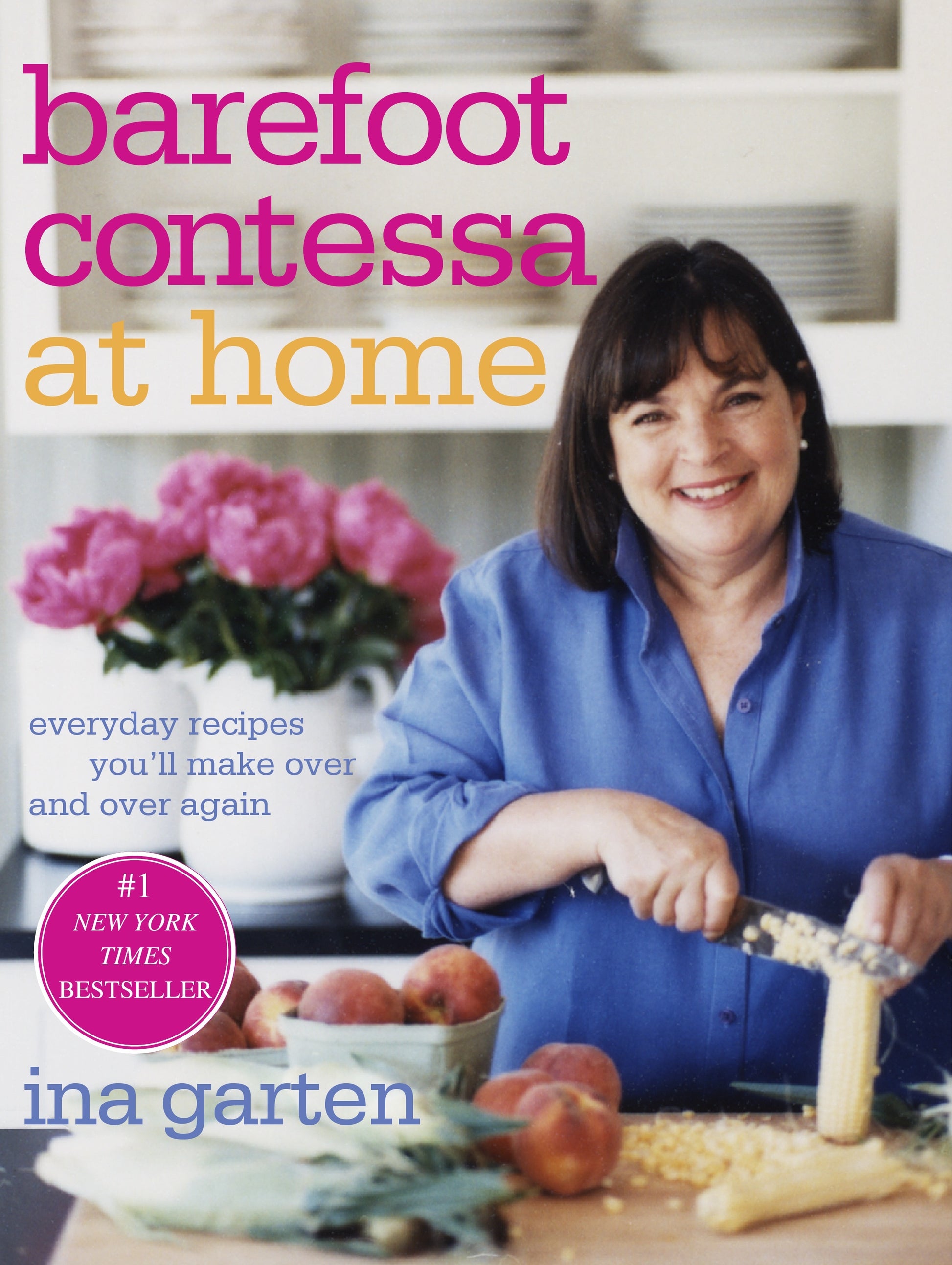 Ina Garten beams as she slices corn on the cover of “Barefoot Contessa At Home” by Penguin Random House, surrounded by fresh peaches and pink flowers—a charming preview of the relaxed, elegant style she brings to her East Hampton kitchen.