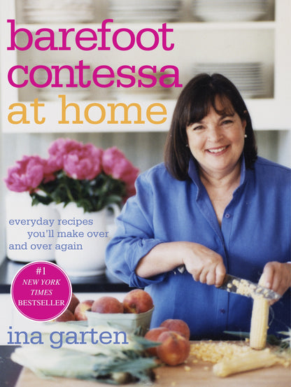 Ina Garten beams as she slices corn on the cover of “Barefoot Contessa At Home” by Penguin Random House, surrounded by fresh peaches and pink flowers—a charming preview of the relaxed, elegant style she brings to her East Hampton kitchen.