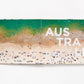 Open Beaches book displaying Gray Malin aerial beach photography of people swimming in turquoise water, with the large white text “AUSTRALIA” printed across the pages.